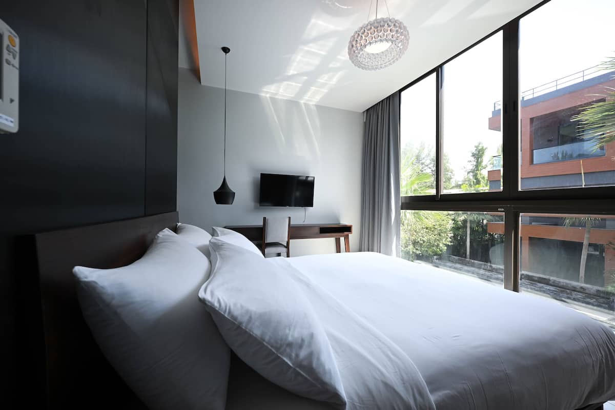 A modern hotel room with a large bed, a desk, a flat-screen TV, and a view of the outside.