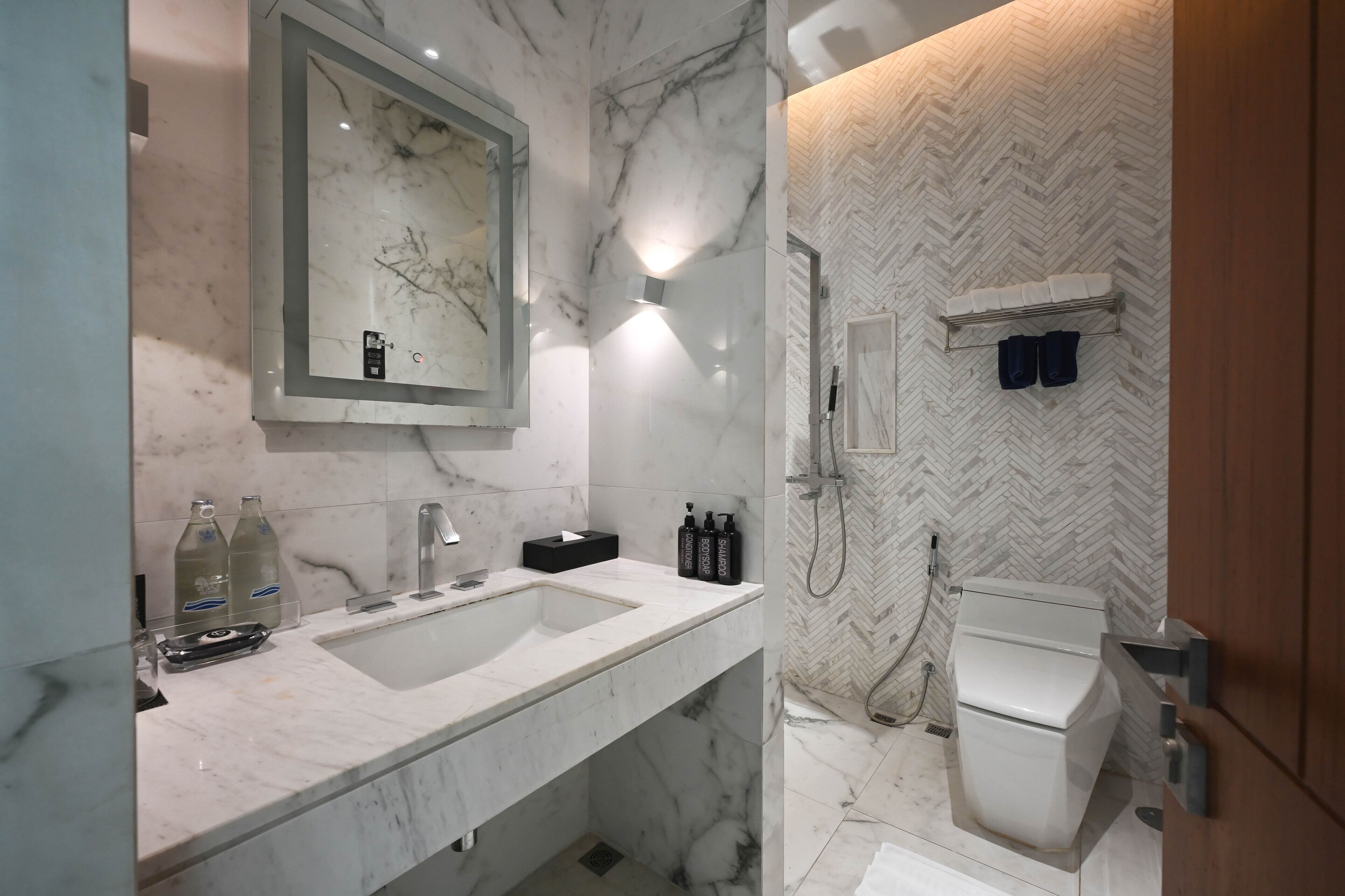 A modern bathroom with a marble sink, a large mirror, and a herringbone-patterned wall.