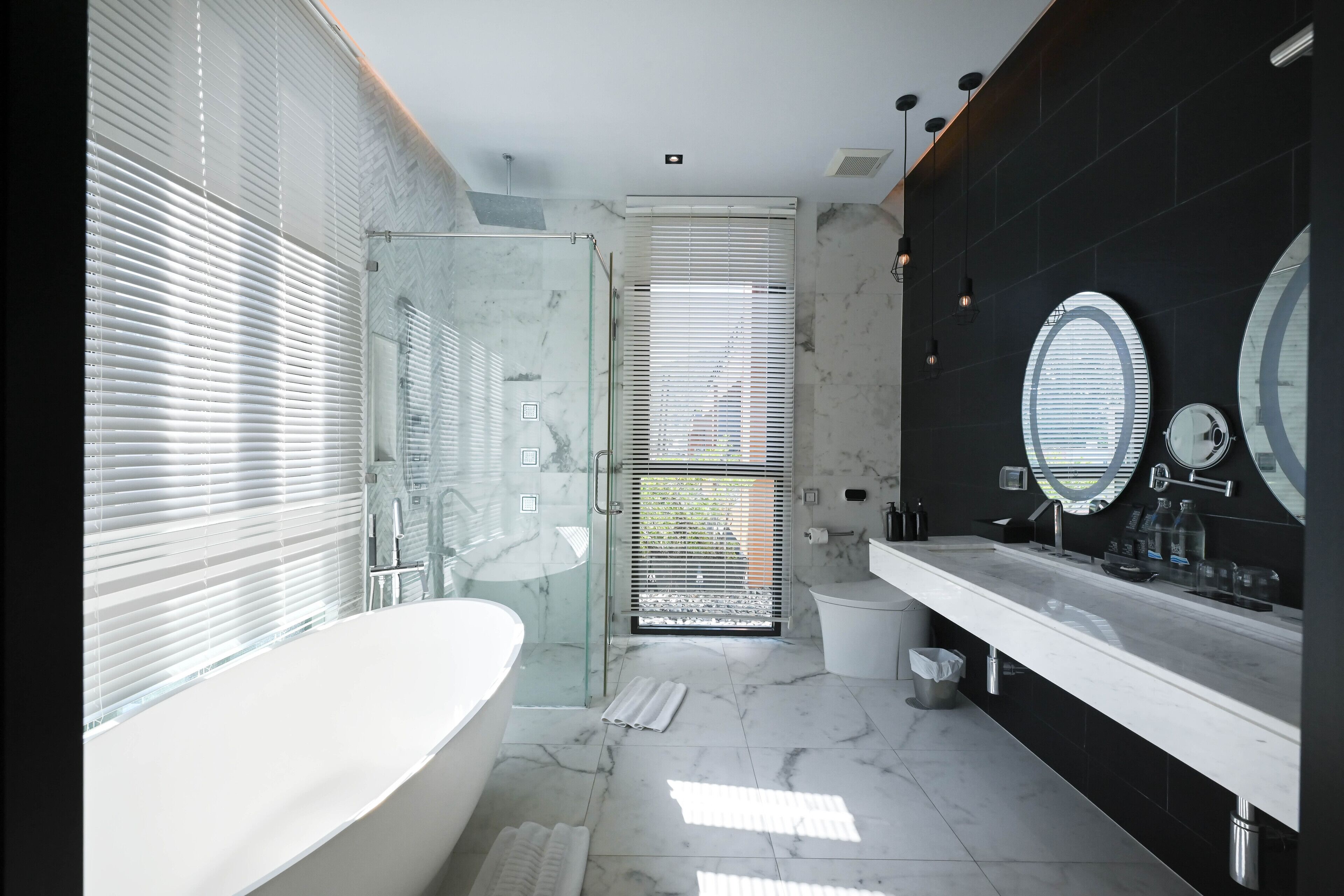 A modern bathroom with a glass shower enclosure, a freestanding bathtub, and a vanity with a large mirror.