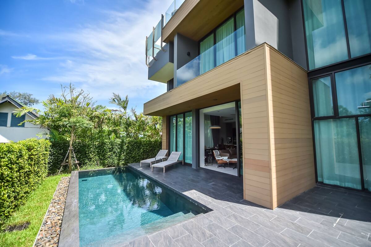 A modern two-story house with a swimming pool, outdoor seating, and large windows.