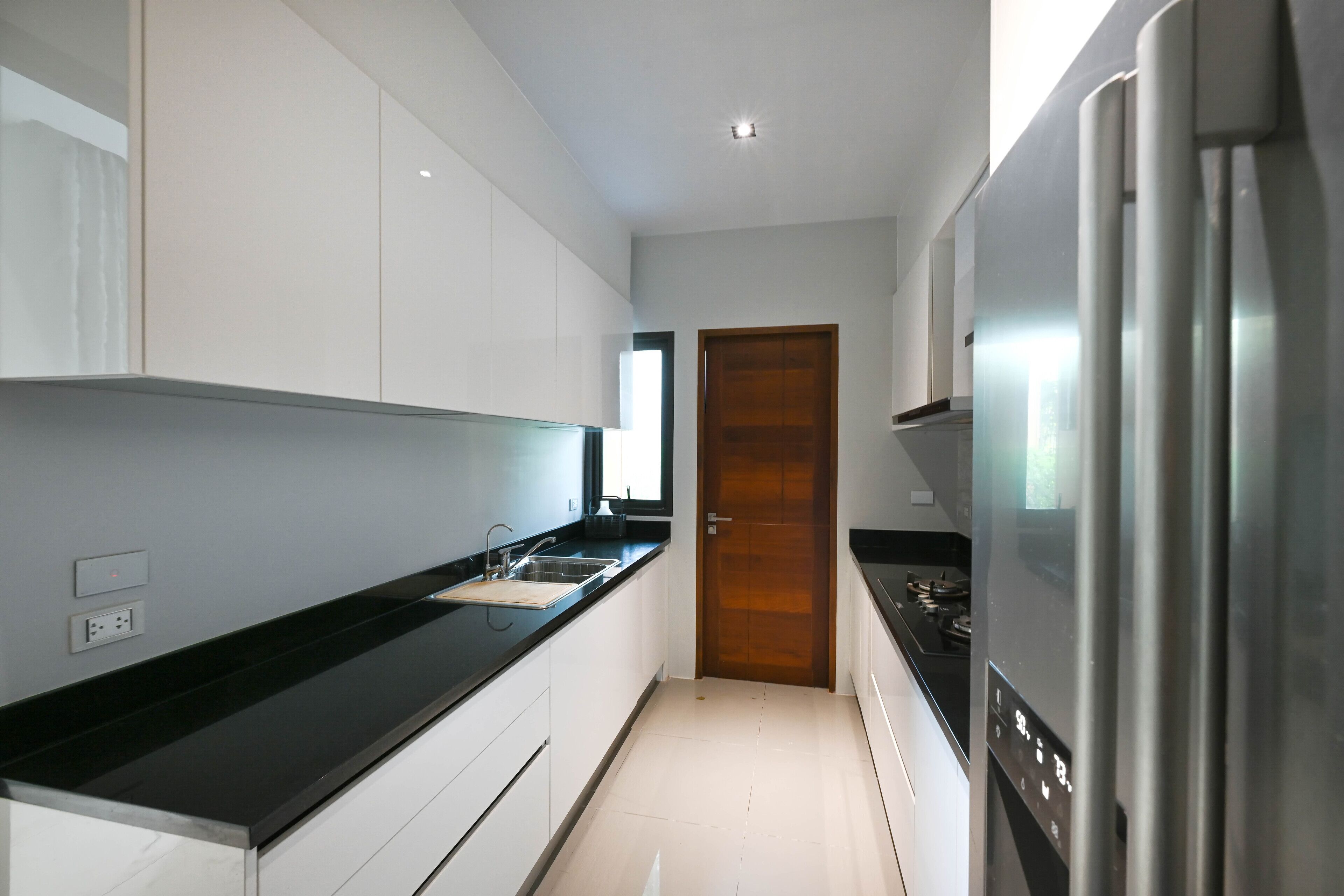 A modern kitchen with white cabinets, a black countertop, a stainless steel refrigerator, and a wooden door.