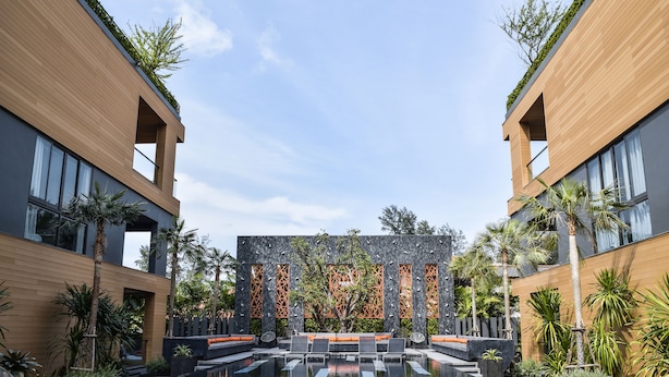 Un edificio moderno con un patio central que cuenta con una piscina reflectante, rodeado de zonas de estar y palmeras.