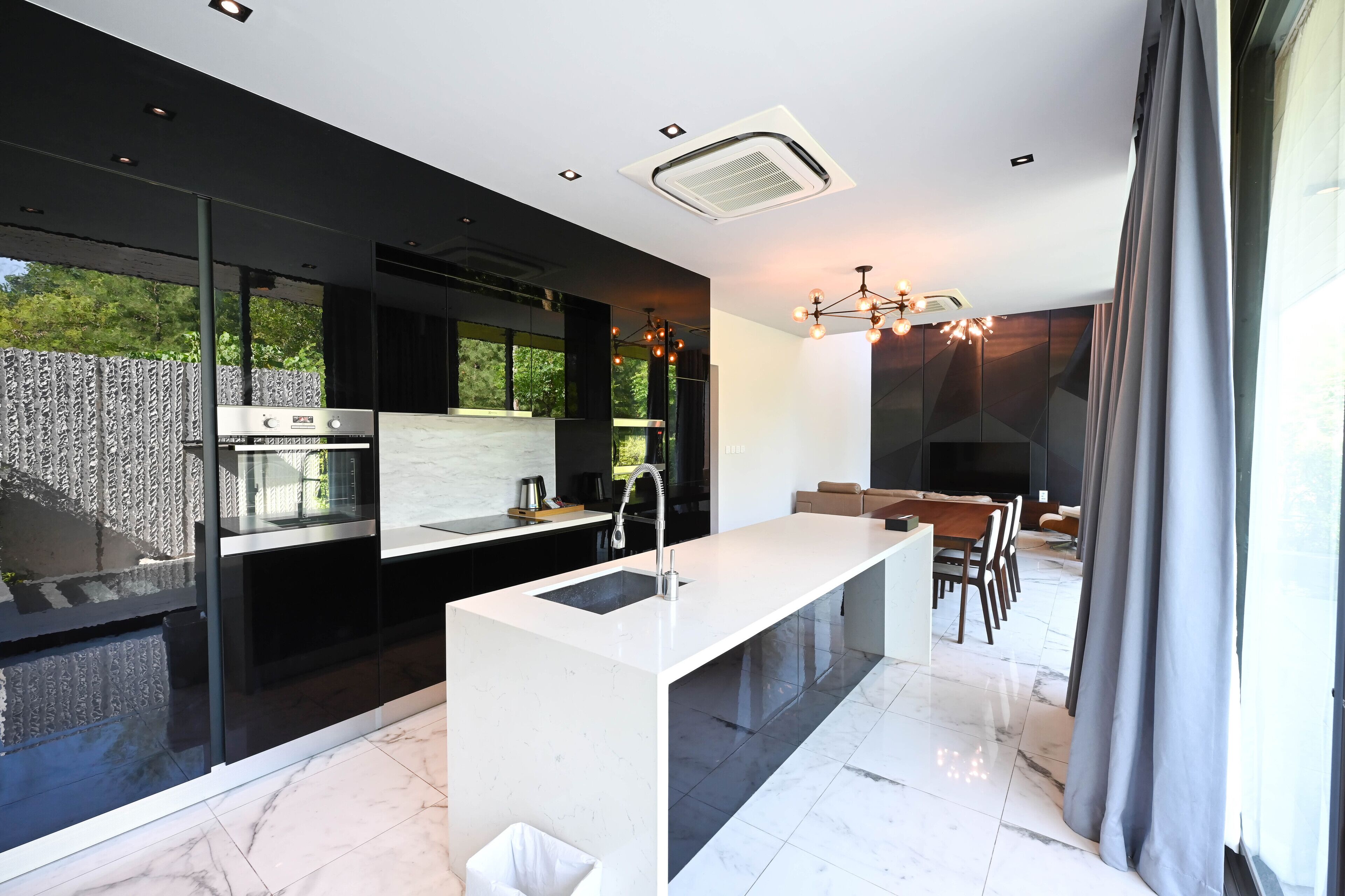 Ett modernt kök med en central köksö, en matplats med bord och stolar samt utsikt över grönområden utanför.