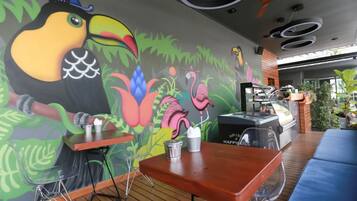 Un restaurante con un mural de un tucán y flamencos, mesas de madera y una zona de parilla.