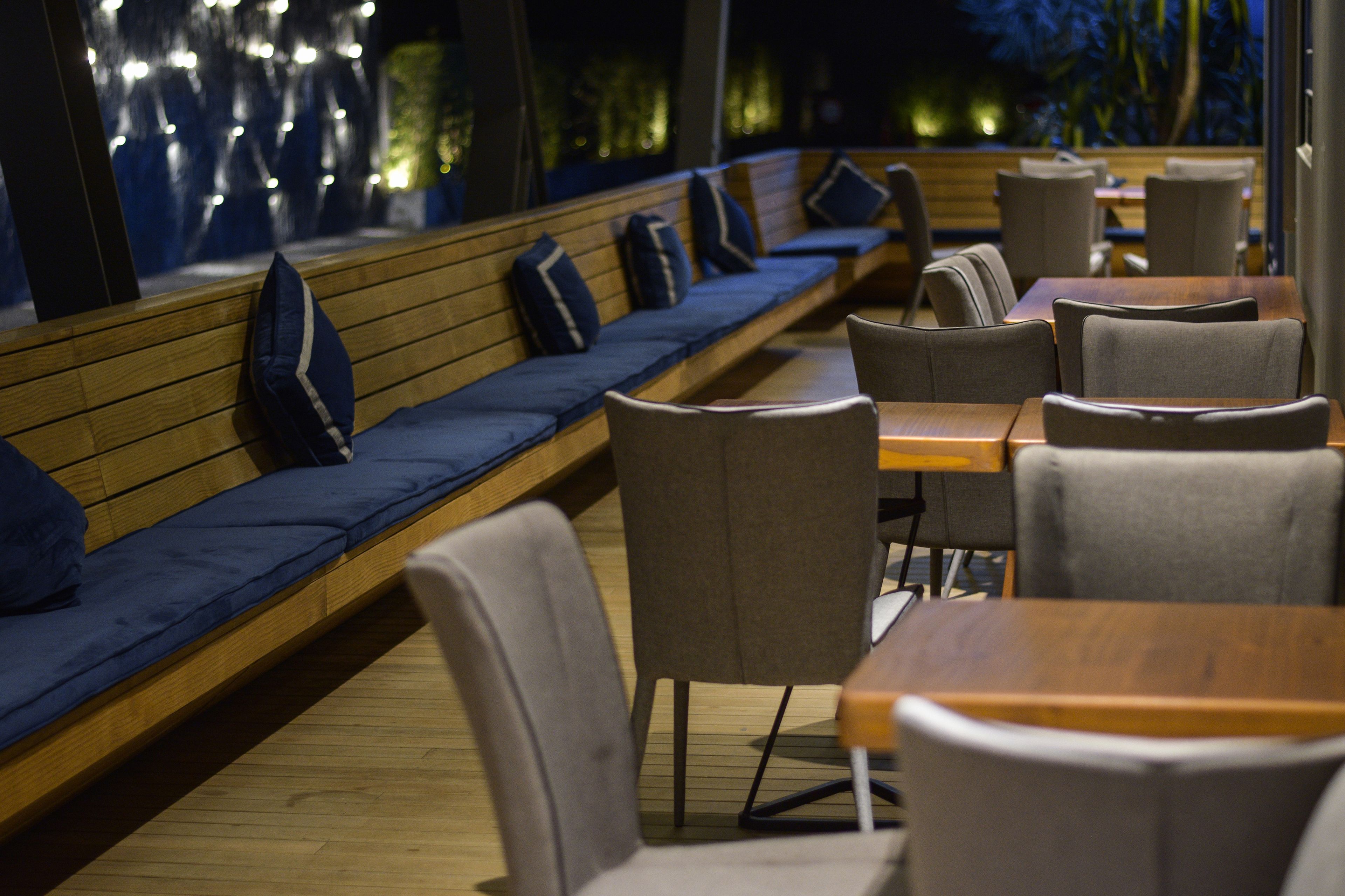 Een restaurant met houten banken en grijze stoelen, tafels en uitzicht op de omgeving.