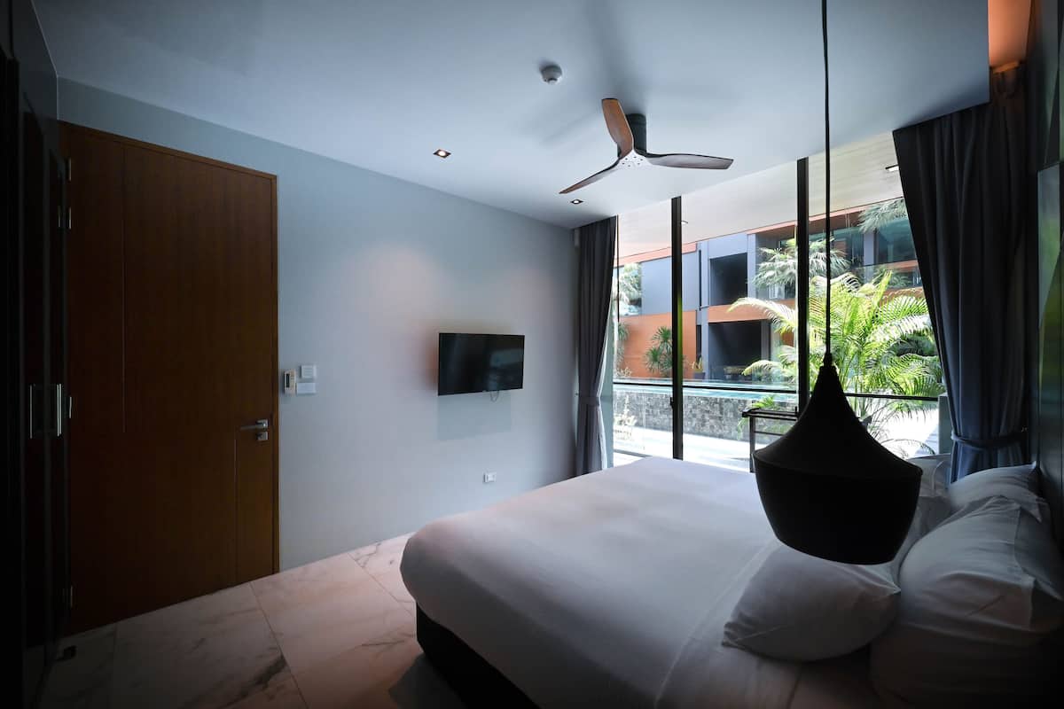 A modern bedroom with a large bed, a ceiling fan, a TV, and a balcony with plants.