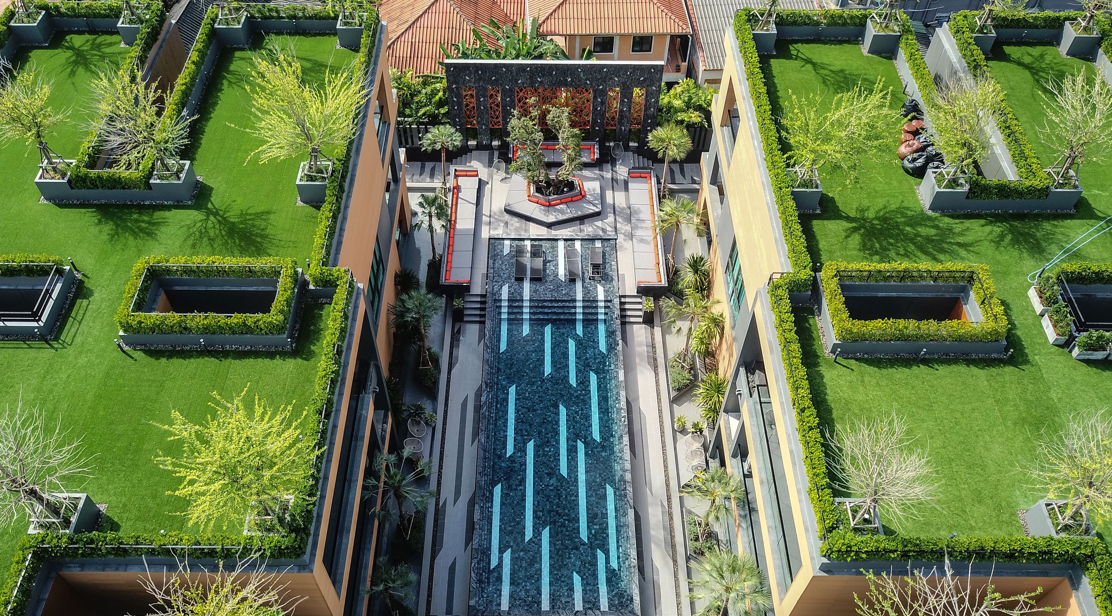An aerial view of a modern building with a central courtyard, surrounded by symmetrical garden beds and a water feature.