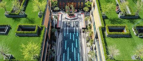An aerial view of a modern building with a central courtyard, surrounded by symmetrical garden beds and a water feature.