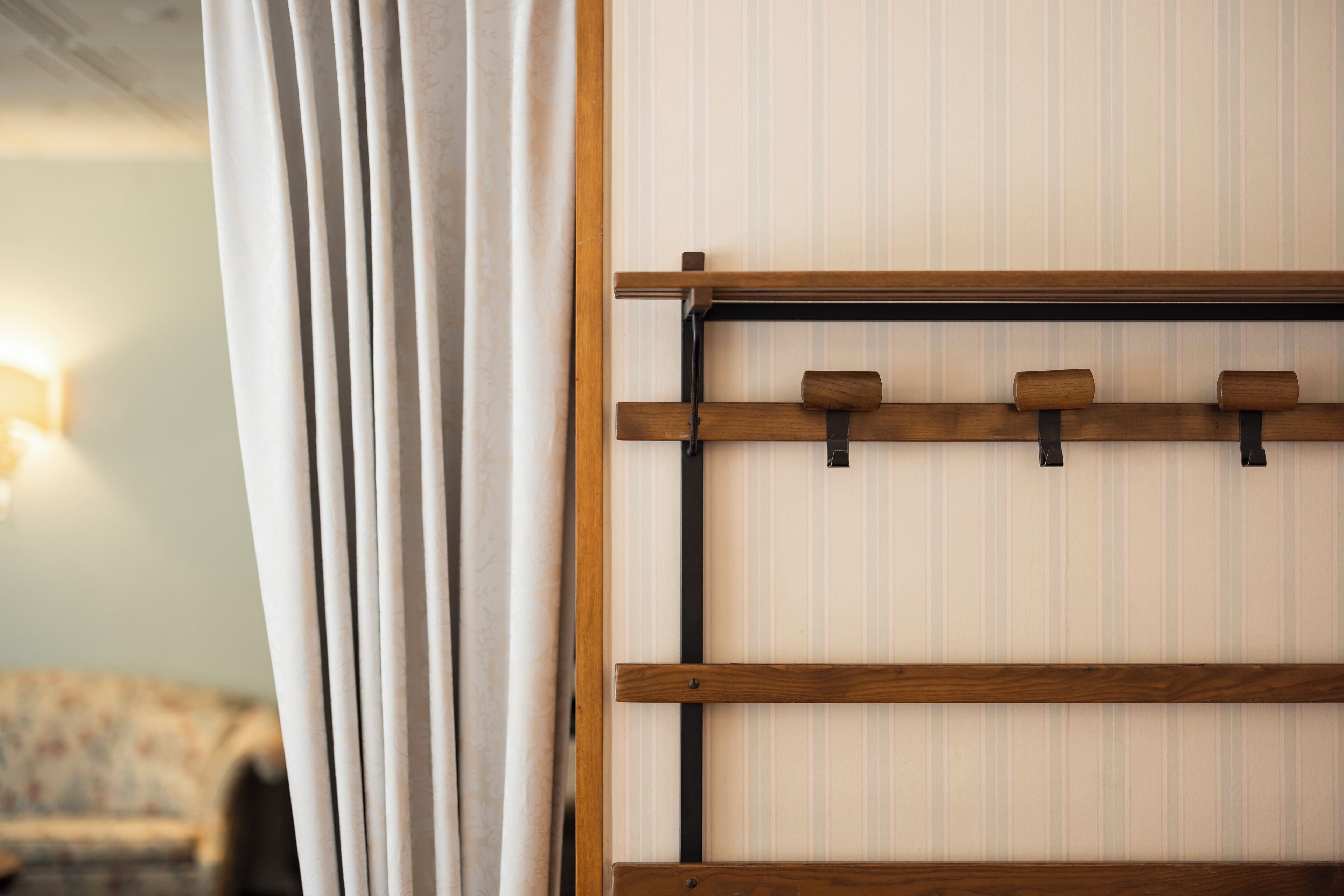 A room with a wooden shelf unit against a striped wall, a curtain partially drawn, and a blurred background suggesting a cozy interior.