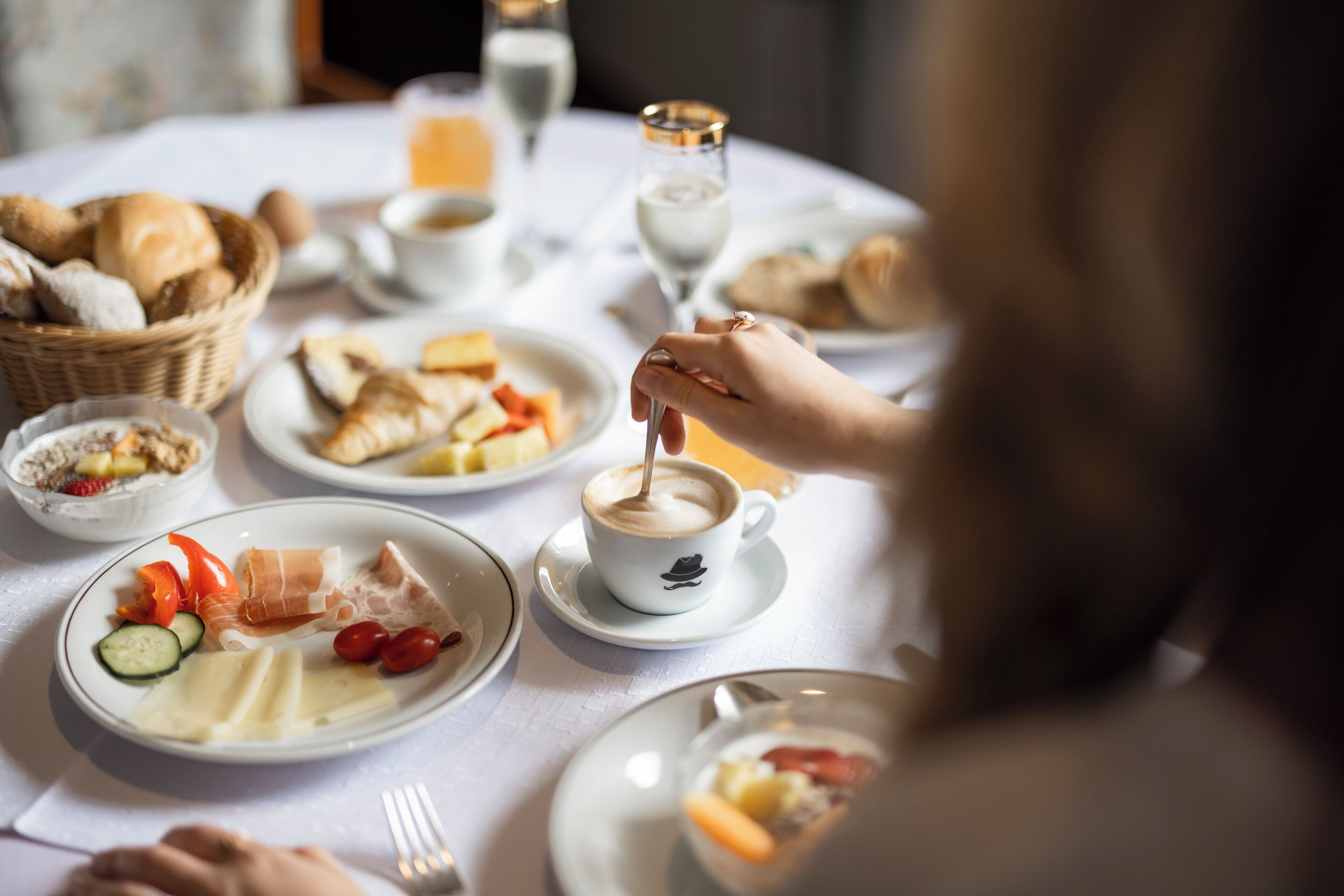 Une table ronde dressée pour le petit-déjeuner, avec différents plats, notamment des croissants, du fromage et du saumon fumé.