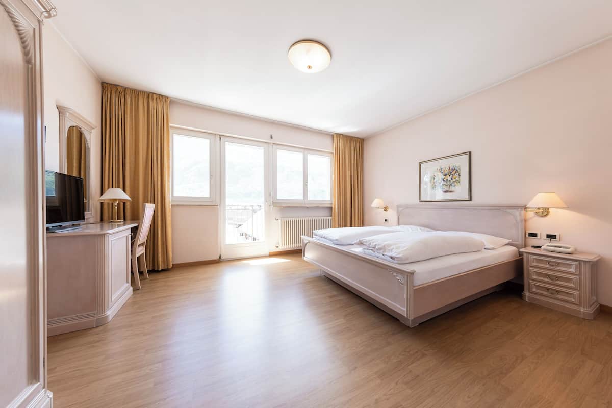 Habitación de hotel con una cama grande, un escritorio con silla, televisión y ventana con cortinas.