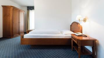 Une chambre d’hôtel comprenant un lit, une armoire en bois, une table de chevet avec une lampe et un téléphone.
