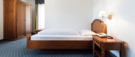 Ein Hotelzimmer mit einem Bett, einem Holzschrank, einem Nachttisch mit Lampe und einem Telefon.