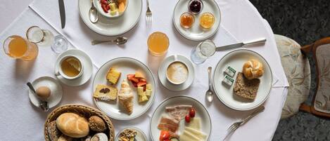 A breakfast setting with various dishes, including bread, fruits, and beverages, arranged on a white tablecloth.