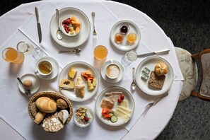 A breakfast setting with various dishes, including bread, fruits, and beverages, arranged on a white tablecloth.