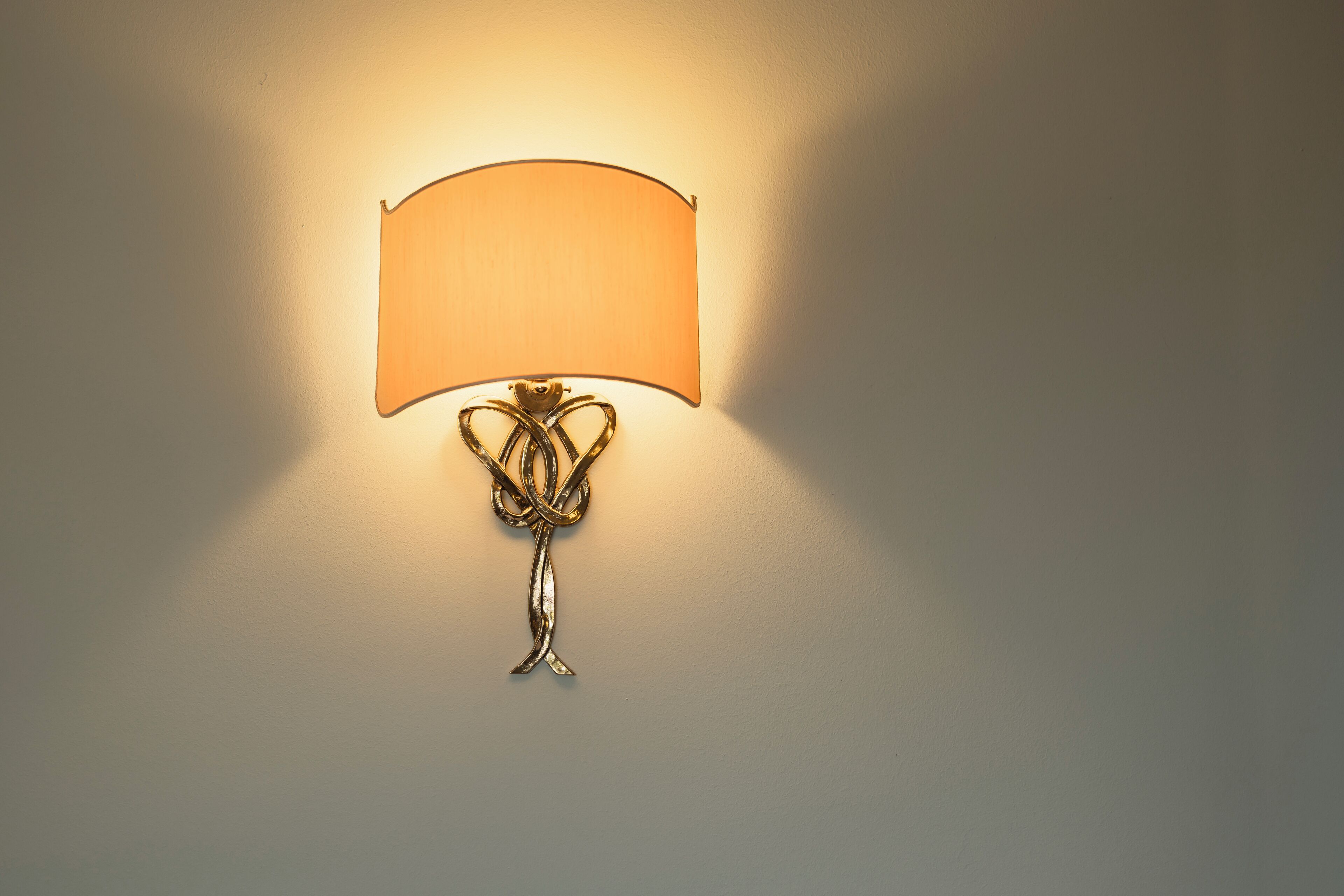 Una lámpara de pared con pantalla curvada y base de metal retorcido.