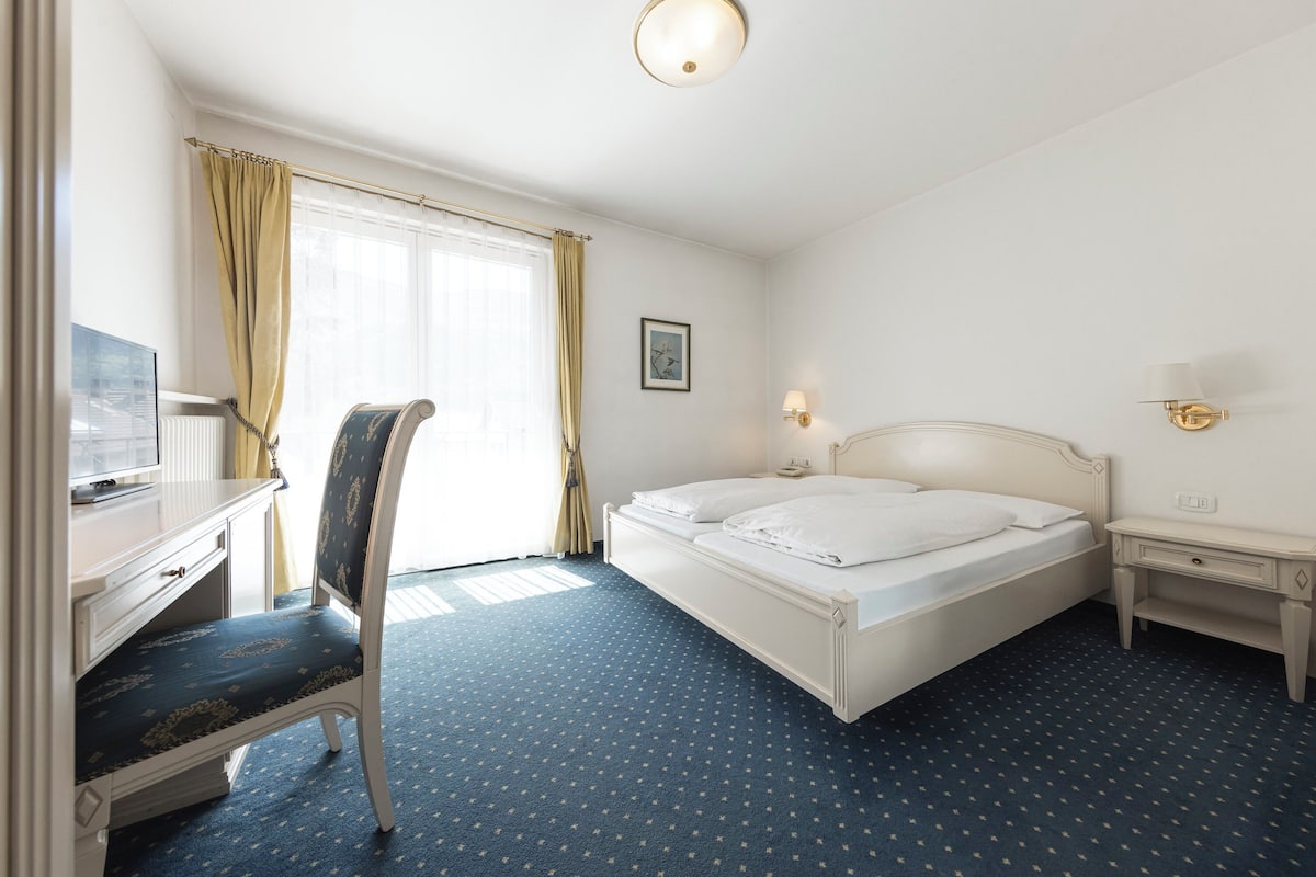 Una habitación de hotel con cama, escritorio, silla, mesita de noche y lámpara.