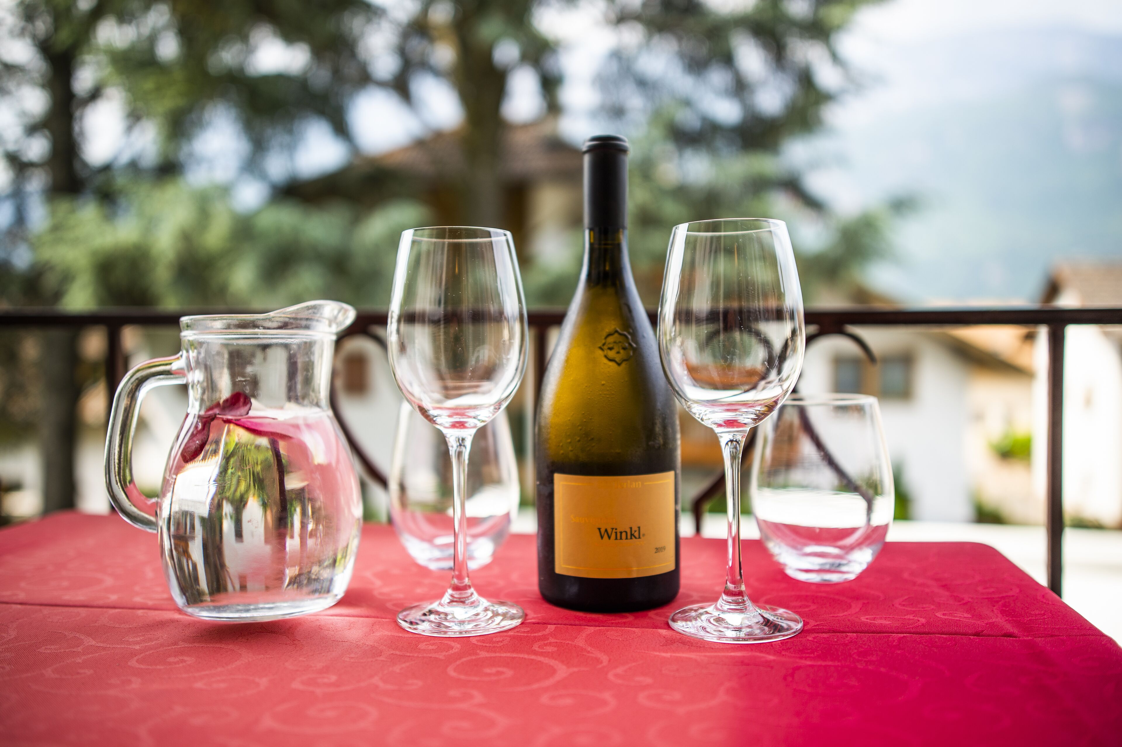 A table with a wine bottle and four wine glasses on a red tablecloth.