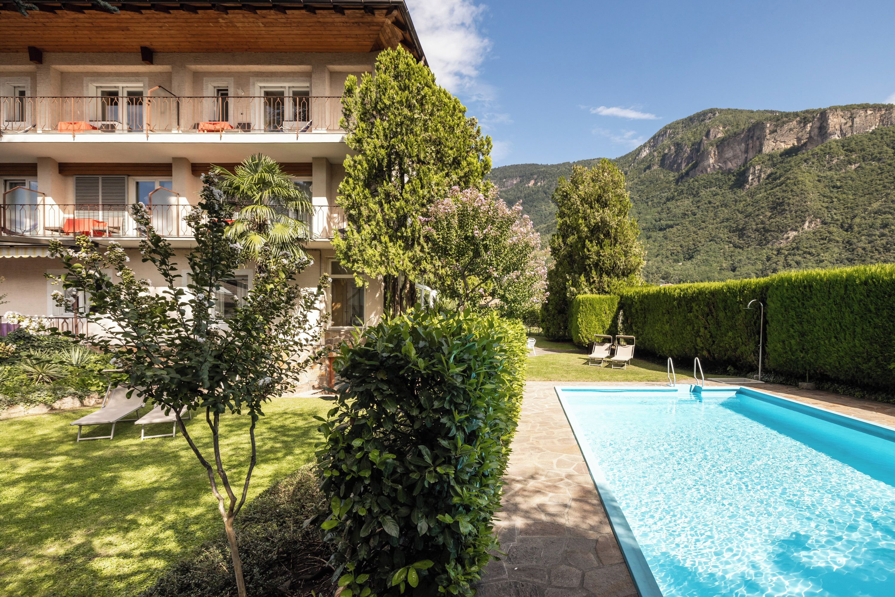 A poolside view of a hotel with a pool, lounge chairs, and a mountainous backdrop.
