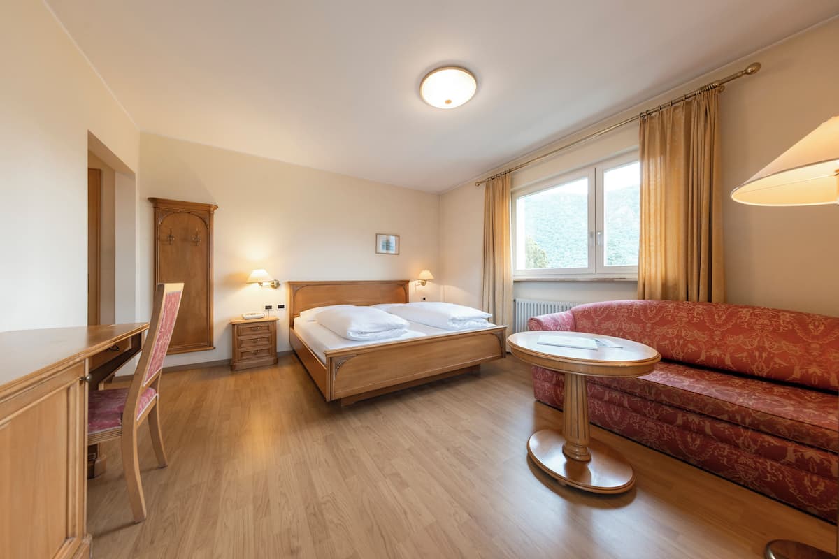 Habitación de hotel con cama de madera, escritorio, sillón, sofá y una pequeña mesa.