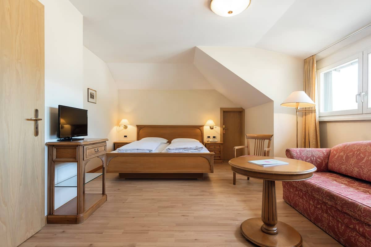 Una habitación de hotel con cama, televisión, escritorio, silla, sofá y lámpara.