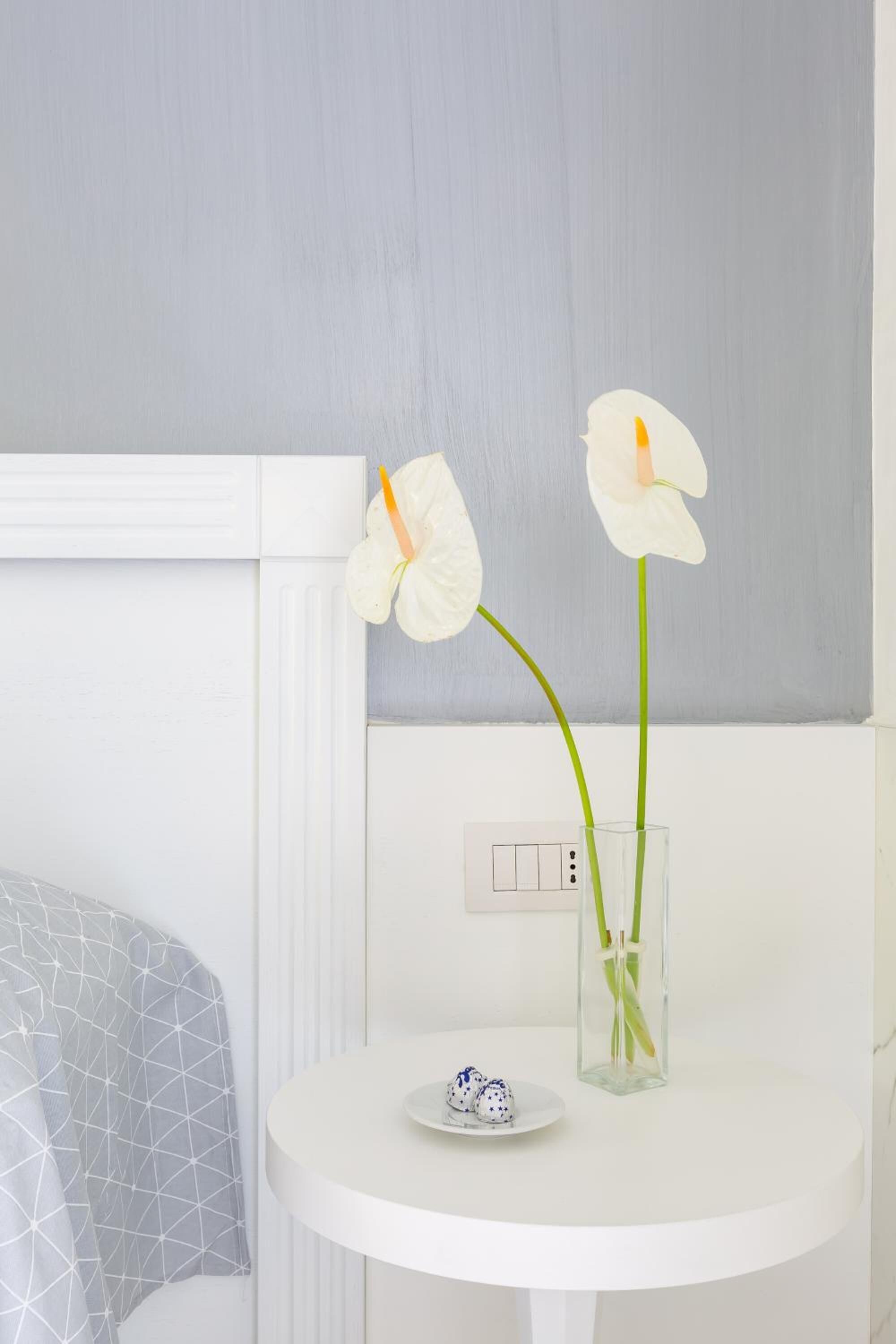 Un meuble-lavabo blanc pour la salle de bain, sur lequel repose un vase en verre contenant deux orchidées blanches et une petite assiette décorative.