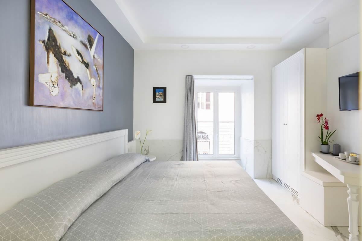 A hotel room with a large bed, a painting on the wall, a television, and a view of the outside.