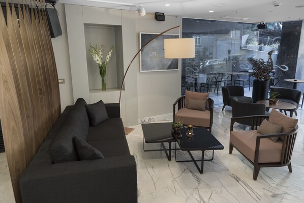 Una sala de estar moderna con un sofá oscuro, sillones, una mesa de centro y un ventanal con vistas a la ciudad.