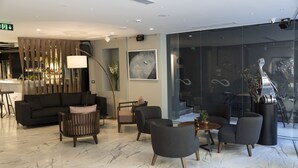 Een moderne lobby met een bank, fauteuils, een bijzettafeltje en een bar.
