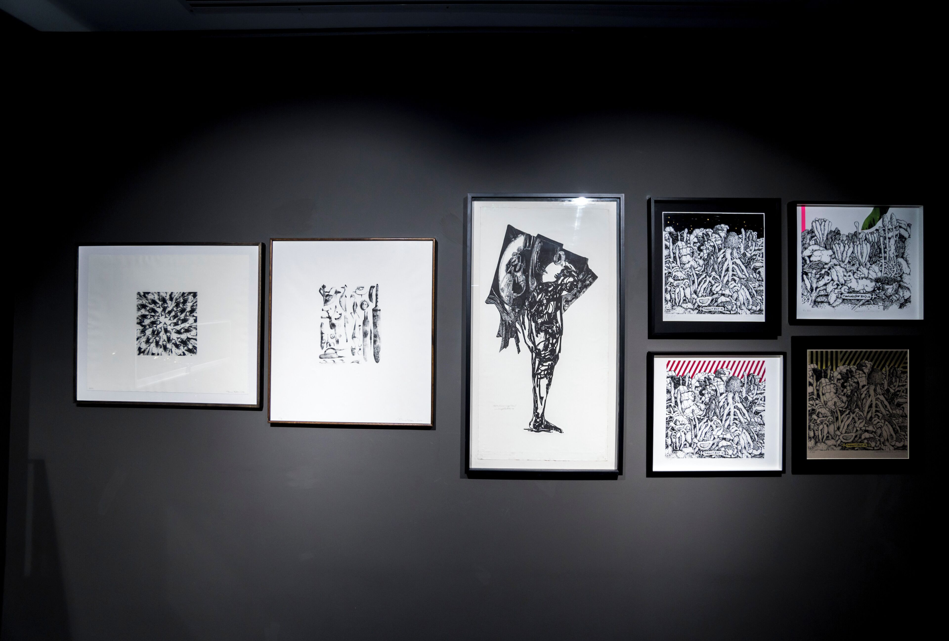 Une galerie où sont exposées six œuvres d’art encadrées sur un mur sombre.