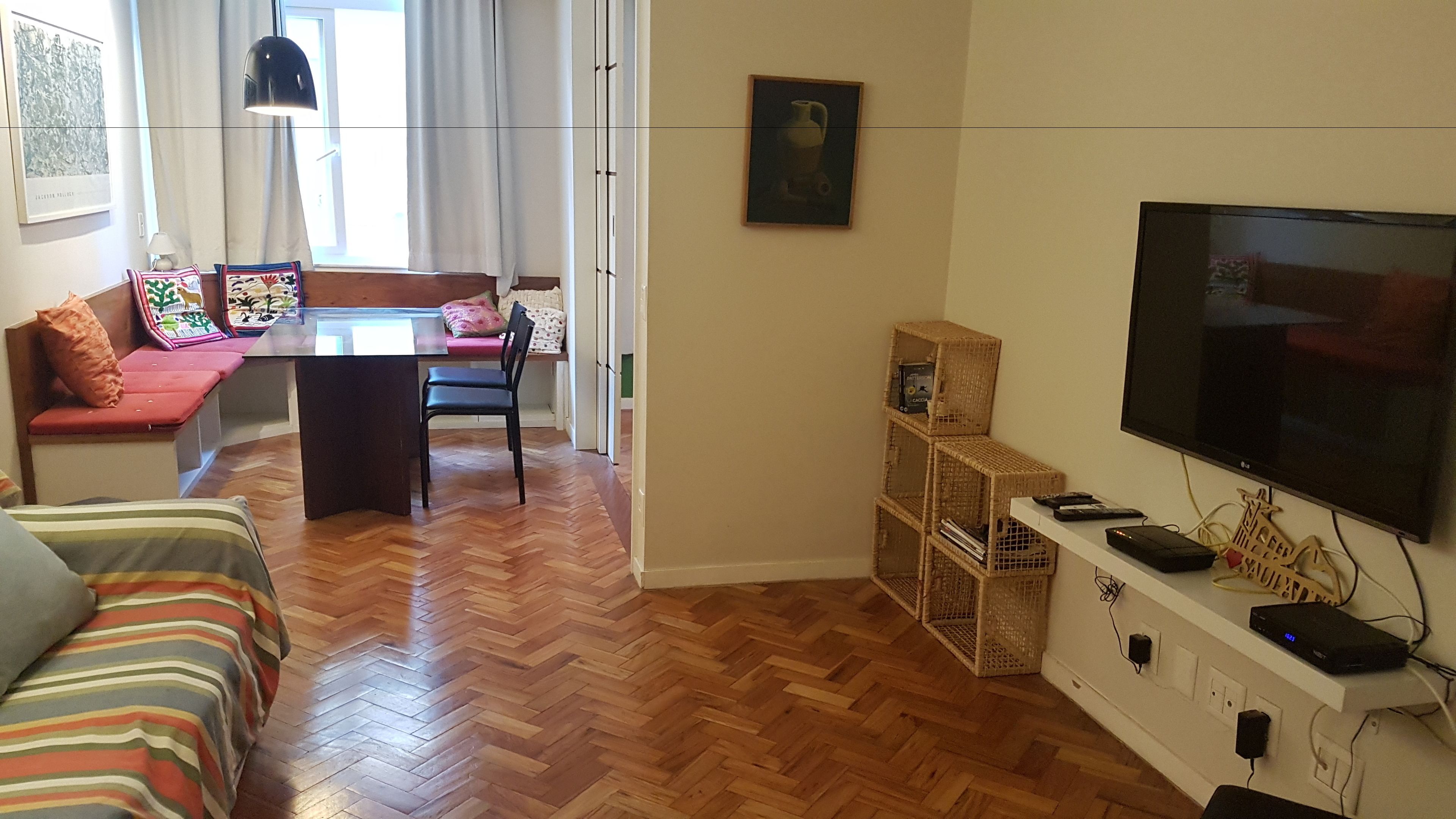 A living room with a herringbone wooden floor, a sofa, a television, and a dining area with a table and chairs.
