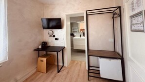 A compact room with a bed, a desk, a television, and a small refrigerator. - dingdong bonn - city apartments (Bonn)