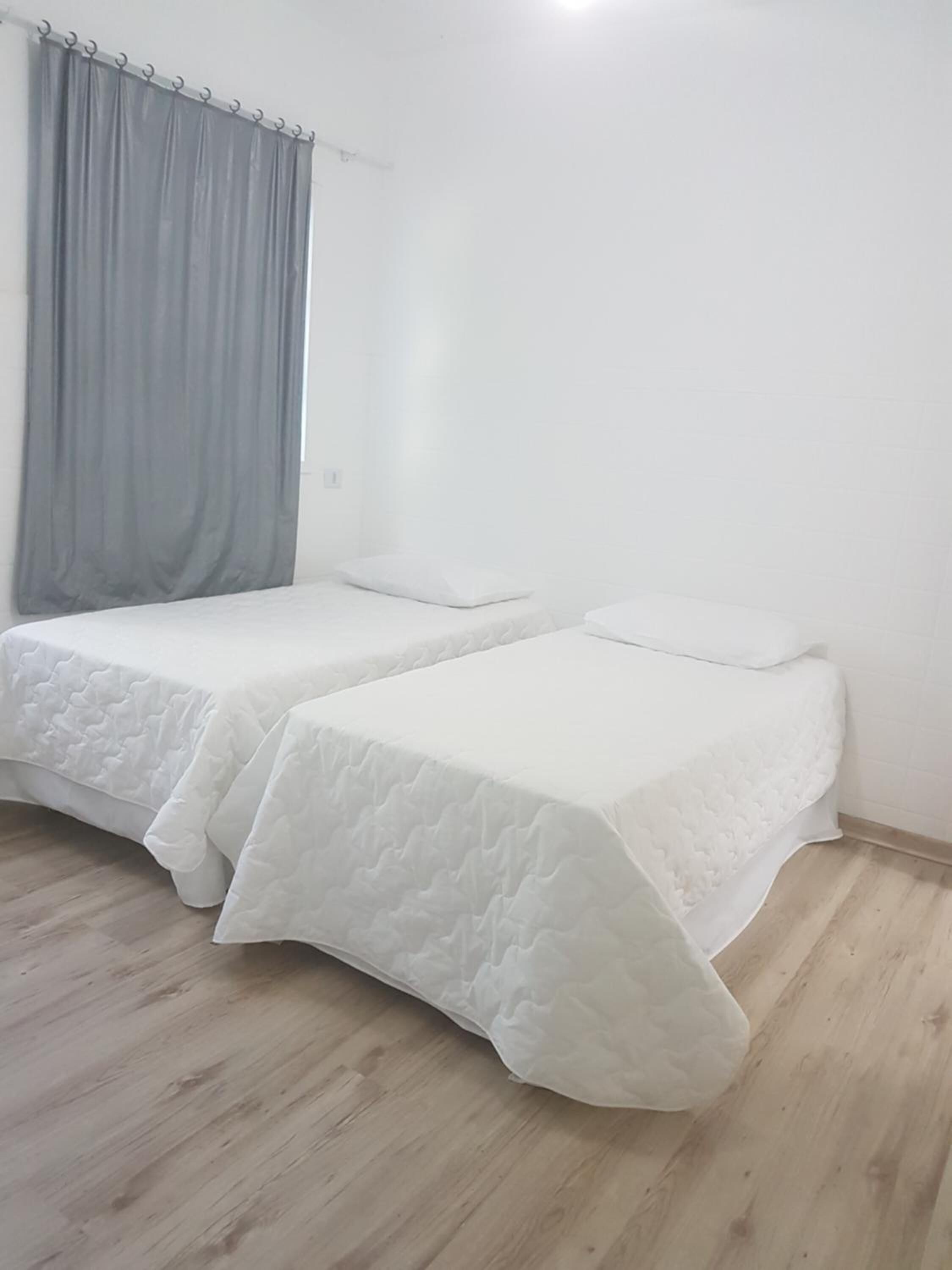 Une chambre avec deux lits simples, un rideau gris et un plancher en bois.