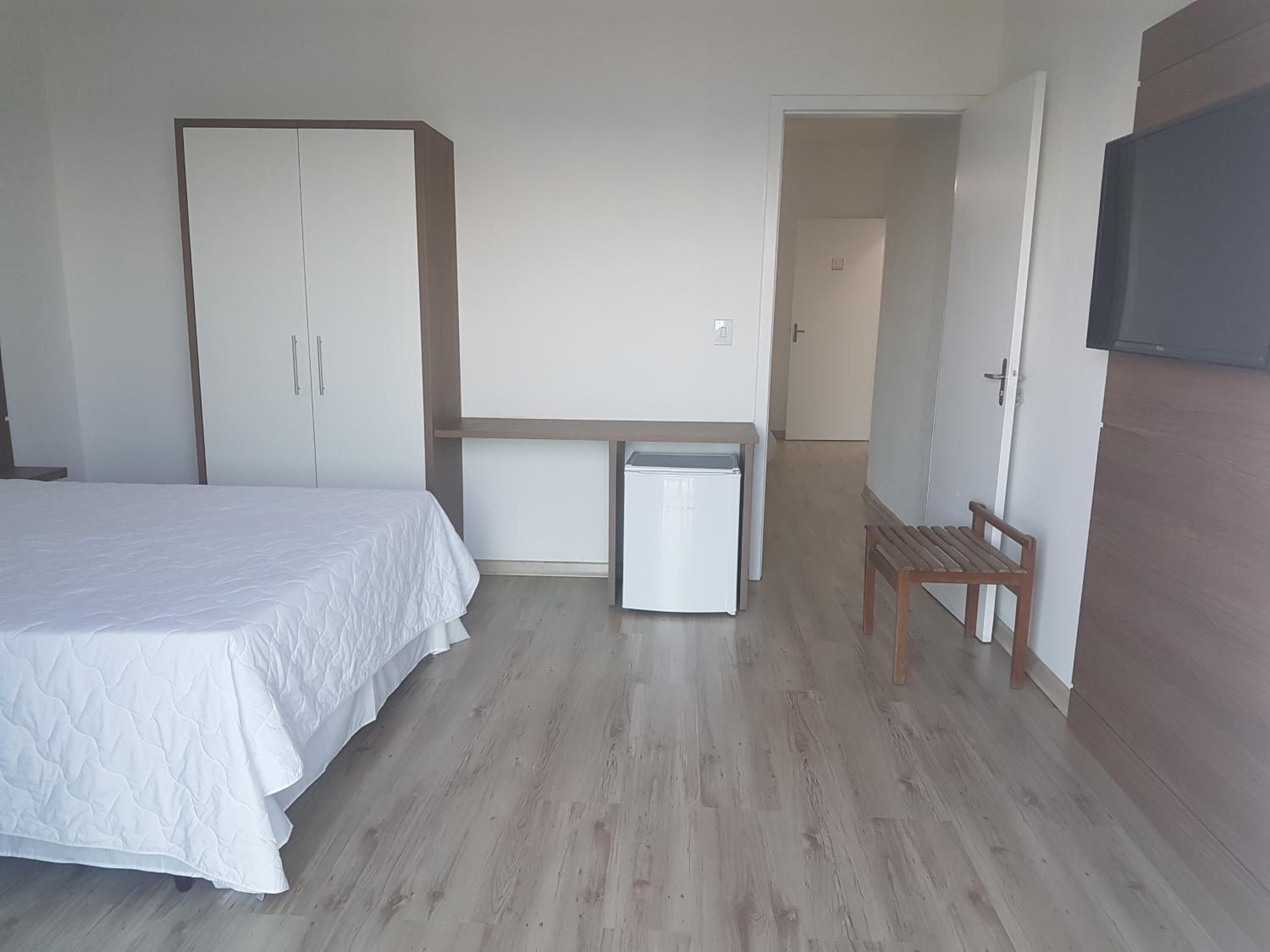 A bedroom with a bed, wardrobe, a small white appliance, and a bench.