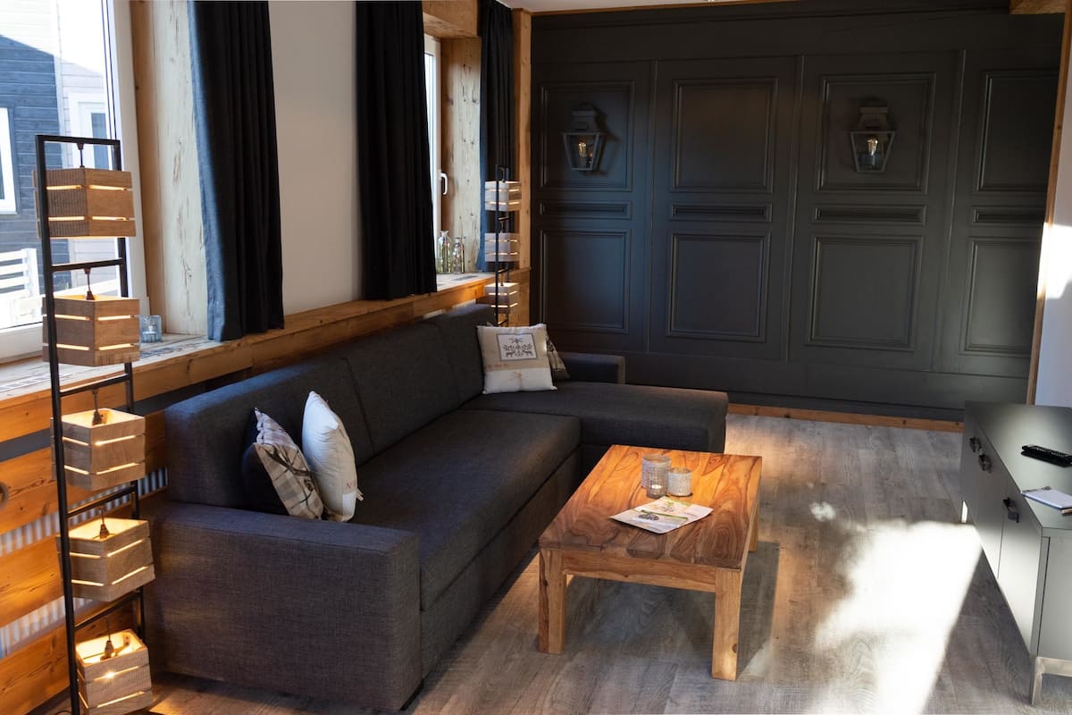 Un salón moderno con un sofá gris, una mesa de centro de madera y una estantería.