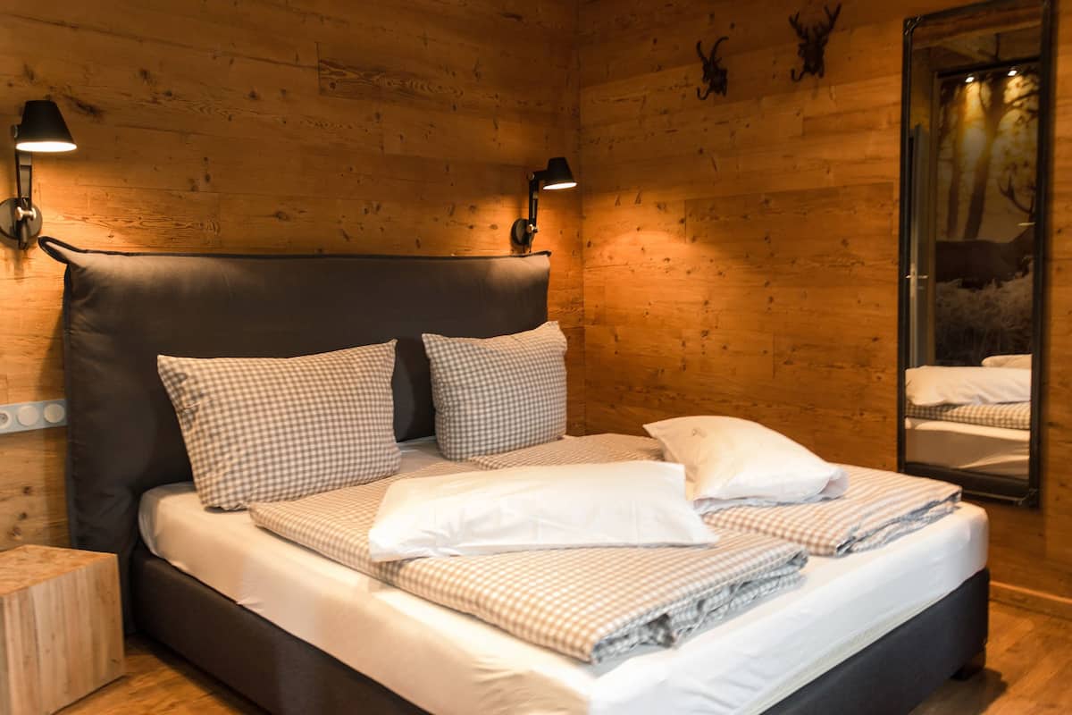 Una habitación con paneles de madera, una cama, dos lámparas de pared y un espejo que refleja el ambiente.