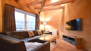 A modern living room with a sofa, a glass coffee table, a TV mounted on the wall, and wooden flooring. - Die Hütten 550 üNN (Braunlage)