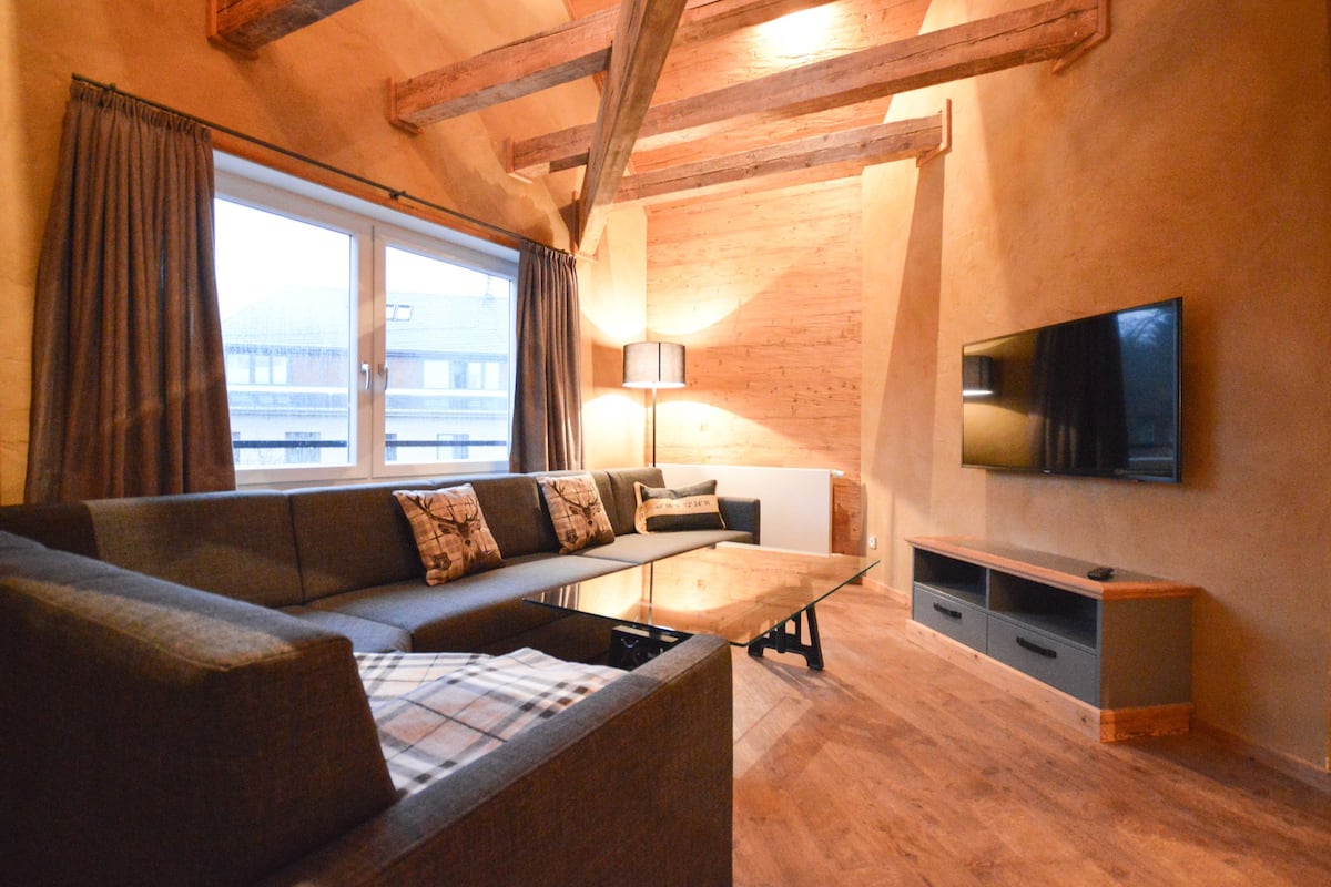Una sala de estar moderna con un sofá, una mesa de centro de vidrio, un televisor montado en la pared y piso de madera.