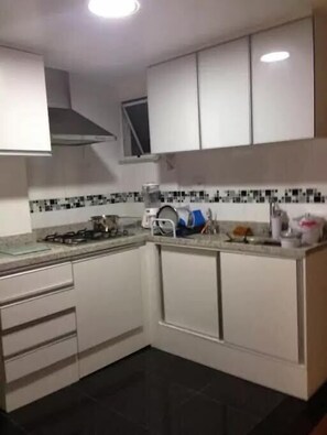 Une cuisine compacte avec des meubles blancs, une cuisinière à gaz, un four à micro-ondes et un dosseret carrelé.