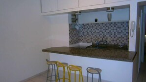 Una cocina pequeña con mostrador, un lavamanos y tres taburetes.