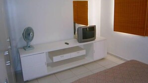 Un dormitorio con un aparador blanco, televisión y ventilador.