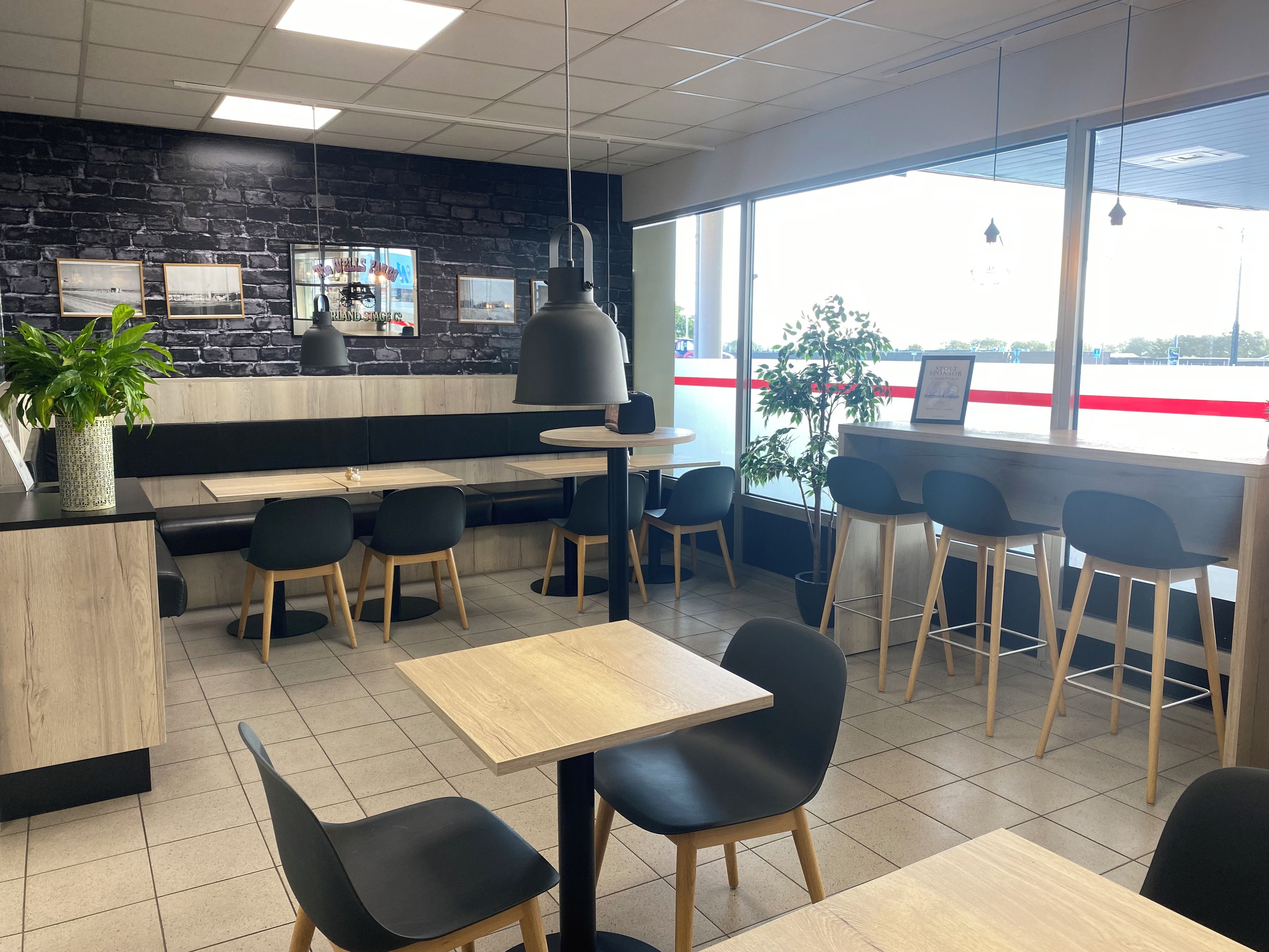 A restaurant interior with black and white decor, wooden tables and chairs, and a view through large windows.