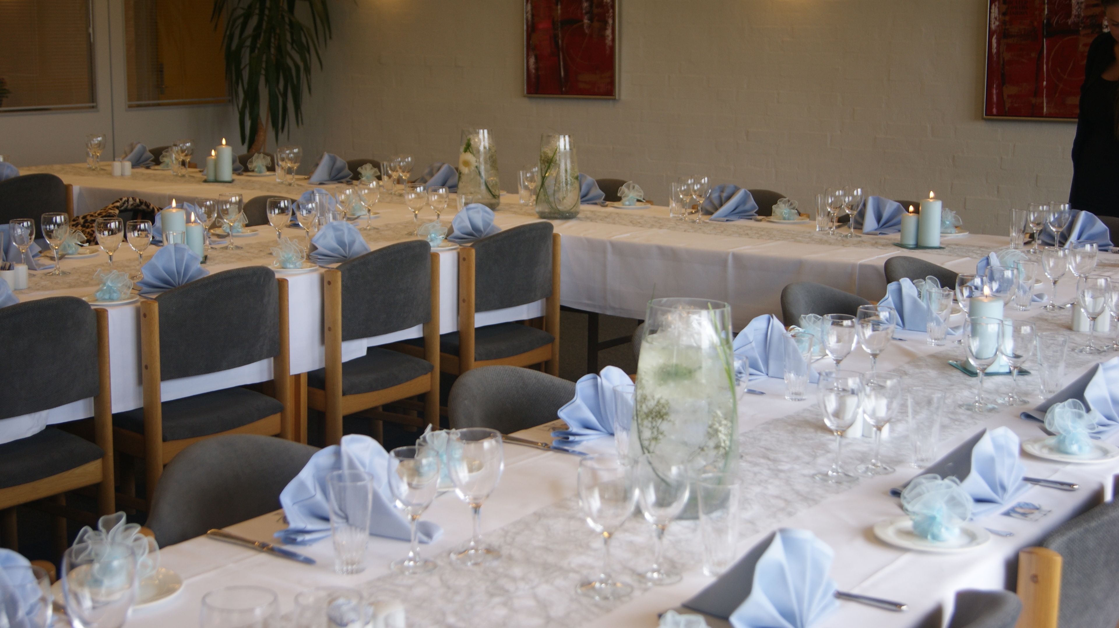 A banquet hall with tables set for a formal event, featuring white tablecloths, glassware, and candles.
