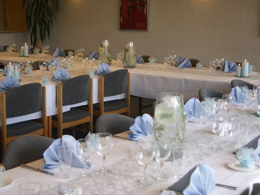 Un salón de banquetes con mesas dispuestas para un evento formal, con manteles blancos, cristalería y velas.