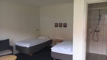 A hotel room with two single beds, a small round table, a chair, and a shower area.