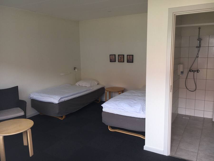 A hotel room with two single beds, a small round table, a chair, and a shower area.