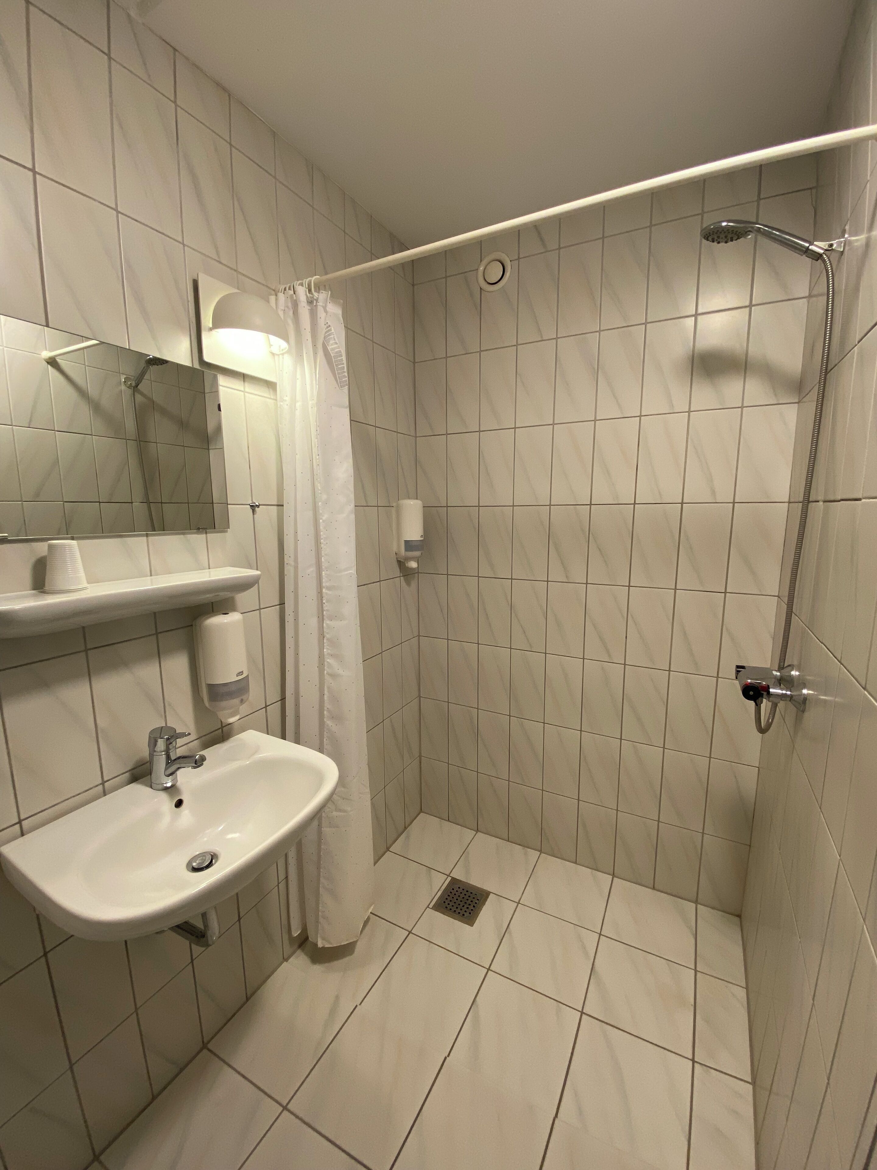 A bathroom with a shower, a sink, a mirror, and a soap dispenser.