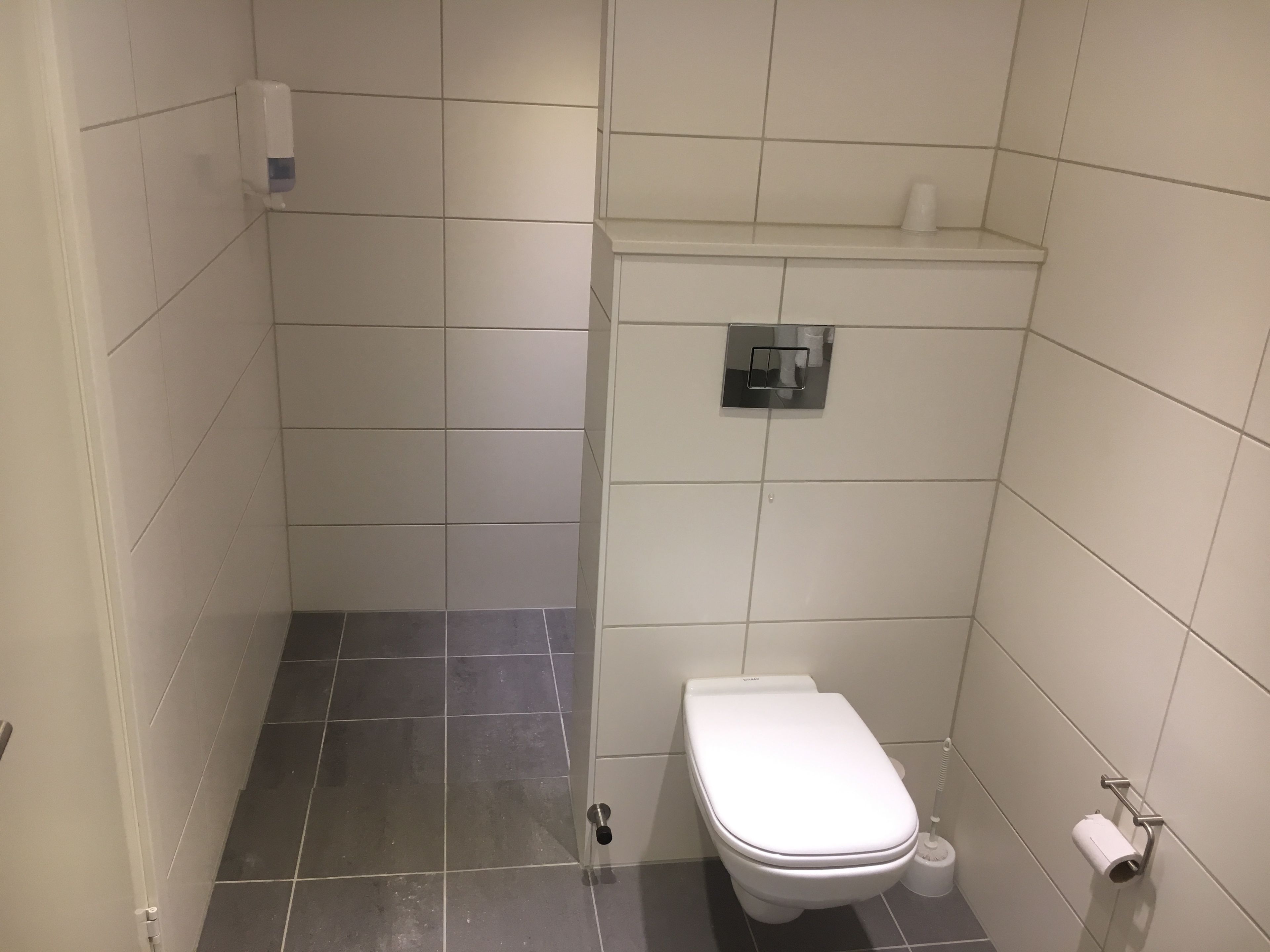 A small, tiled bathroom with a toilet, a hand dryer, and a toilet paper holder.