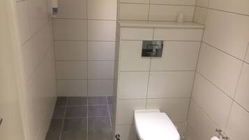 A small, tiled bathroom with a toilet, a hand dryer, and a toilet paper holder.