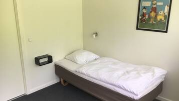 Quarto pequeno com uma cama de solteiro, parede simples, um quadro emoldurado e mesa de cabeceira.
